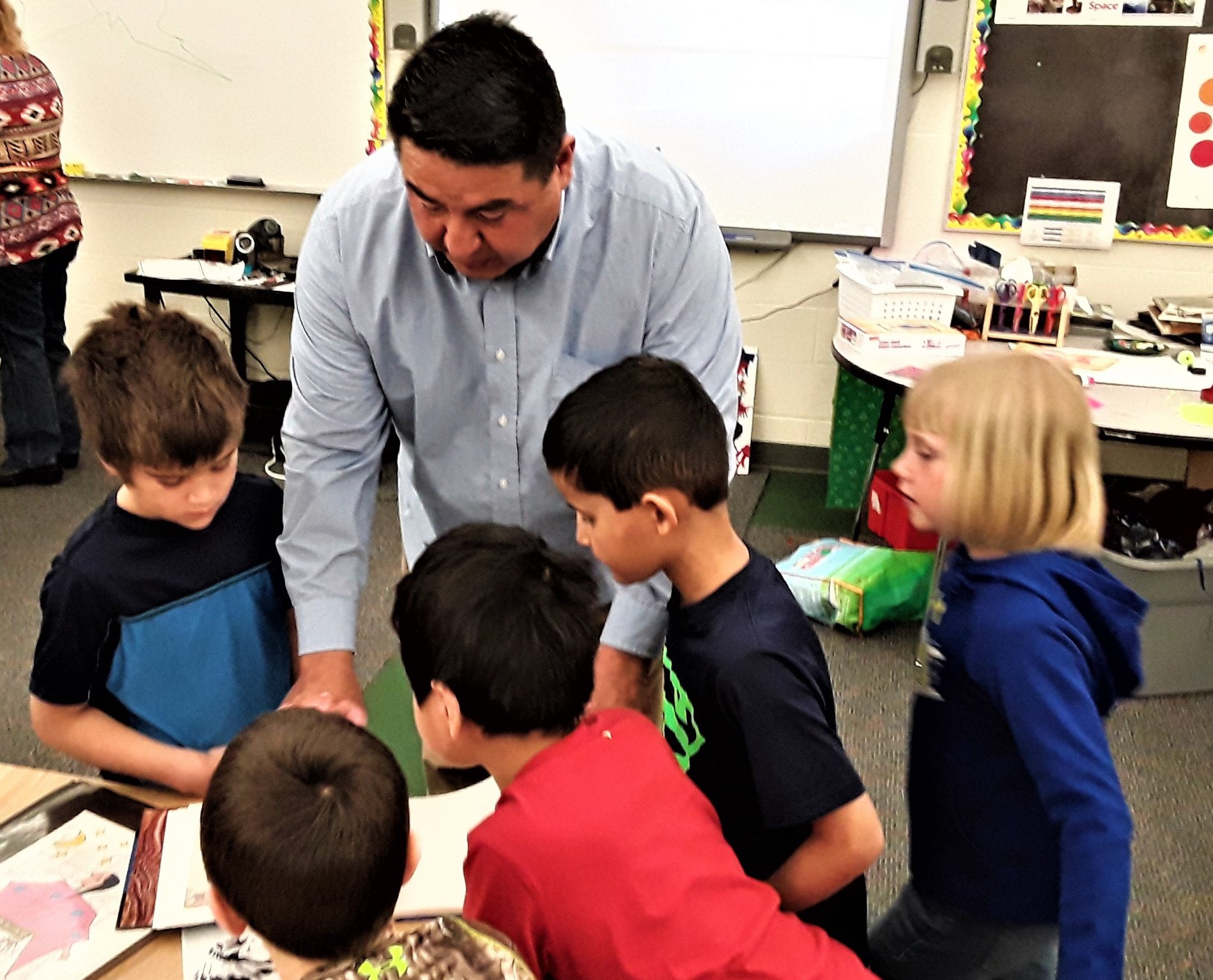 A man surrounded by 5 kids in a classroom