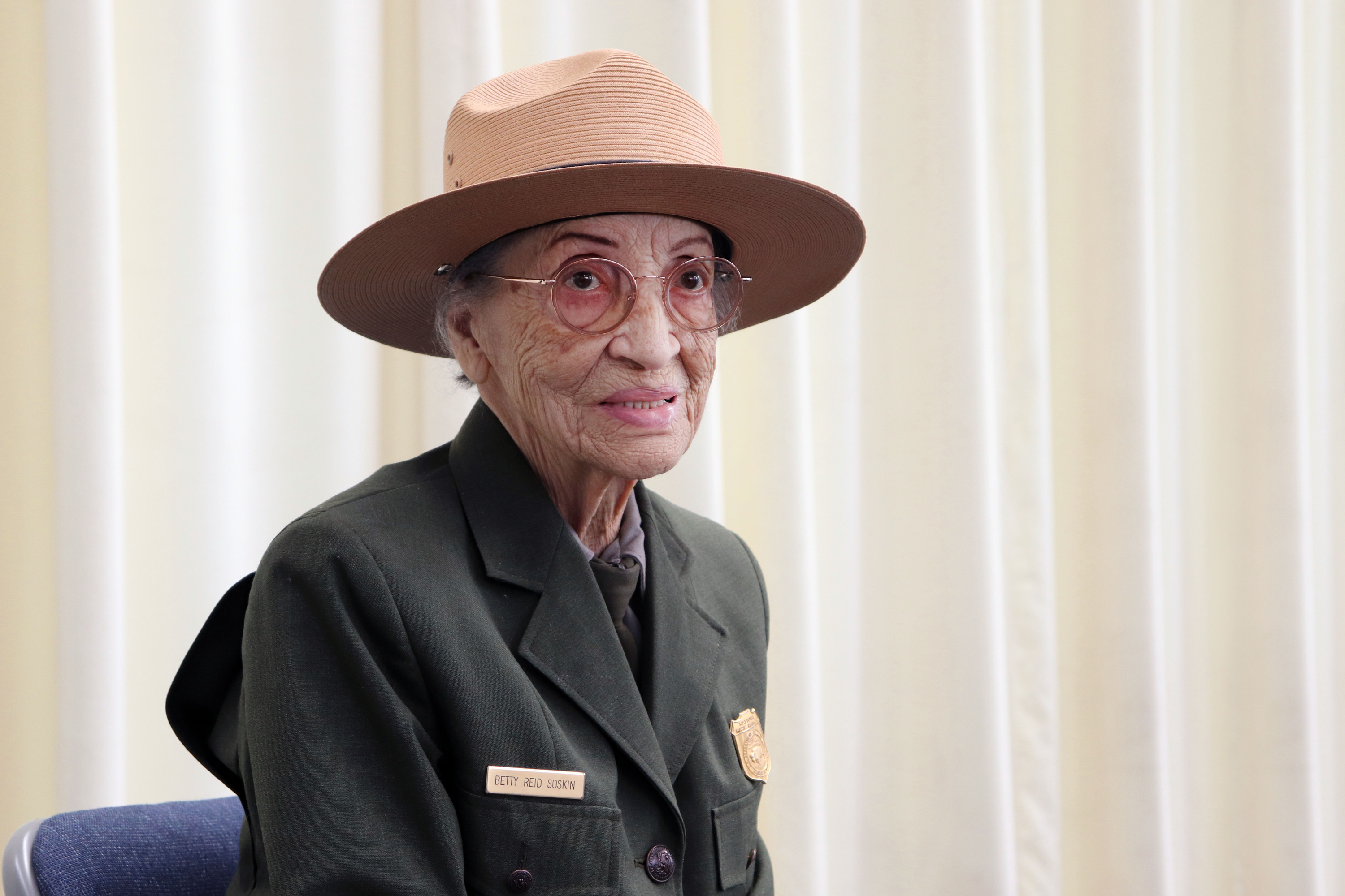 A senior African American woman in a ranger uniform sits in chair. 