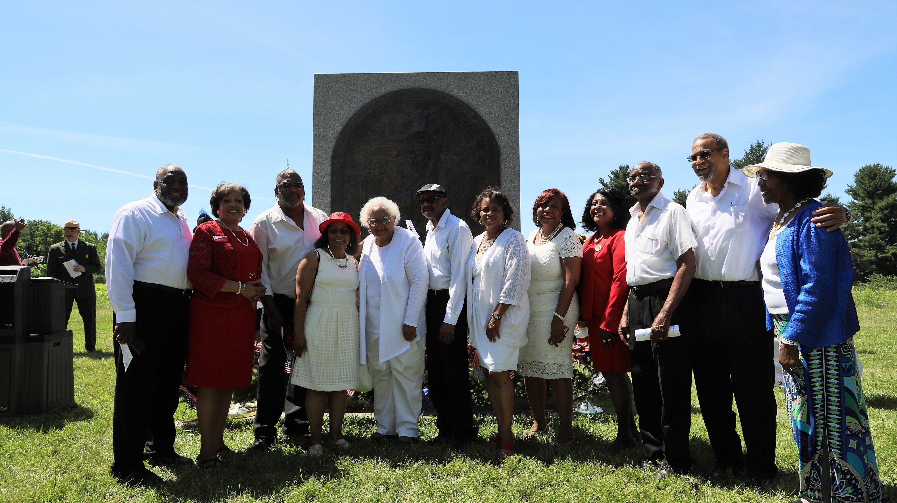 outdoors, twelve people in foreground, monument in back, smiling