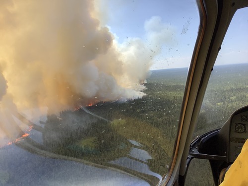 aerial view of smoke rising from a spruce forest near a wide river. reflected flames can be seen in the canopy of the aircraft