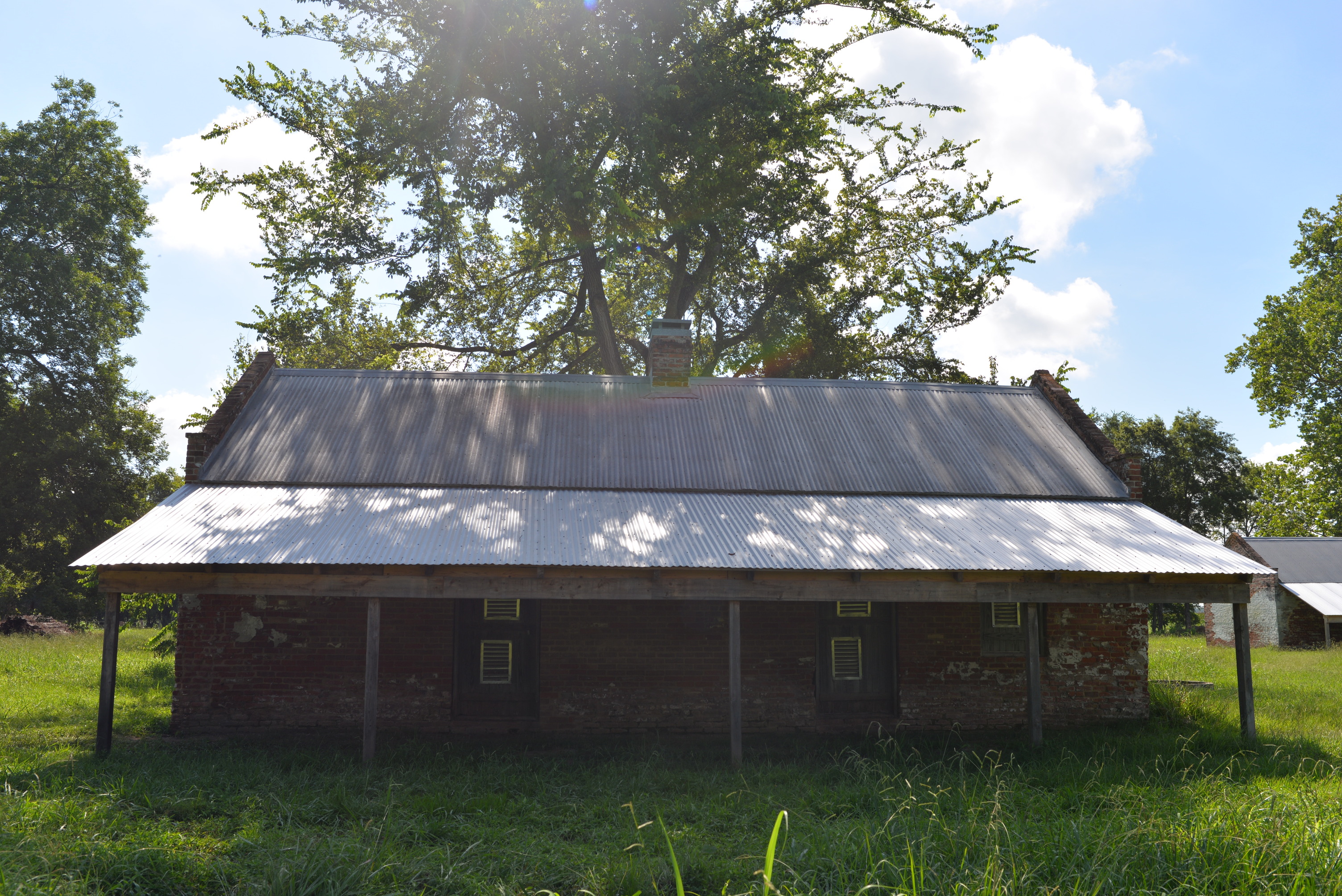 Straight on view of brick structure, a chimney centrally located, and metal roof with awning.