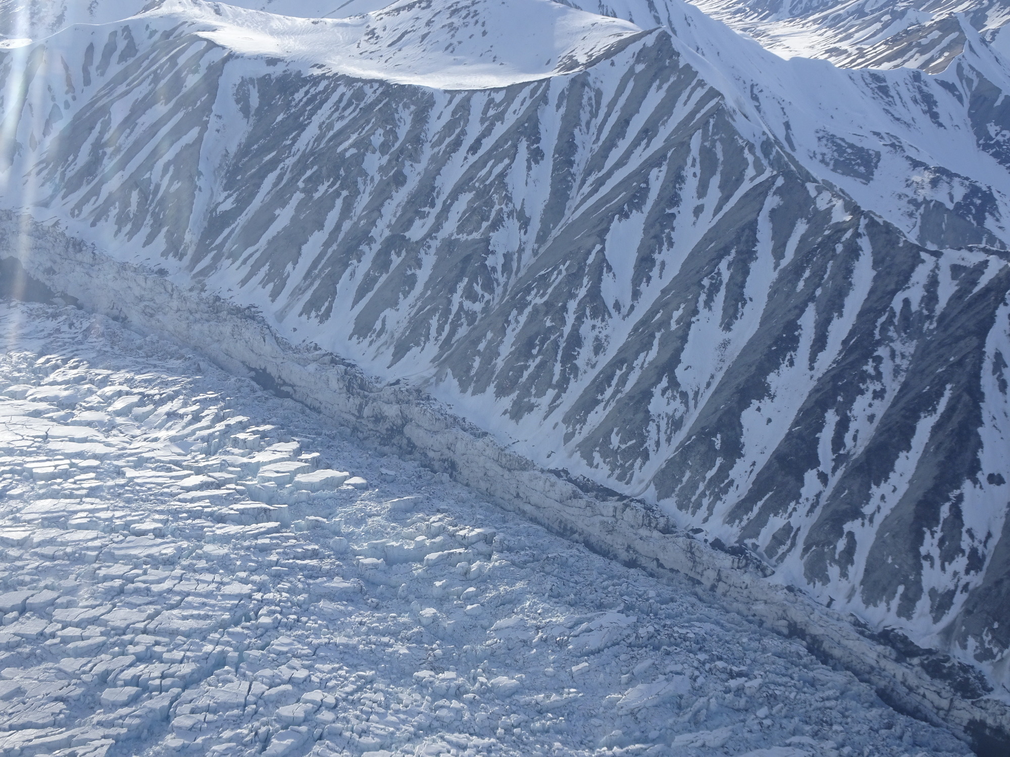 aerial view of a glacier at the foot of a mountain, with trenches in the ice where the glacier and mountain touch