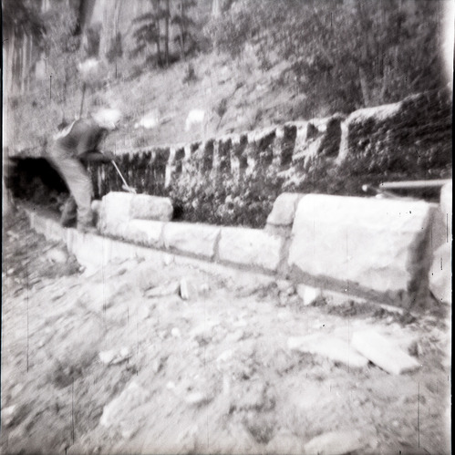 Man working on rebuilding rock retaining wall alongside road at the tunnel.