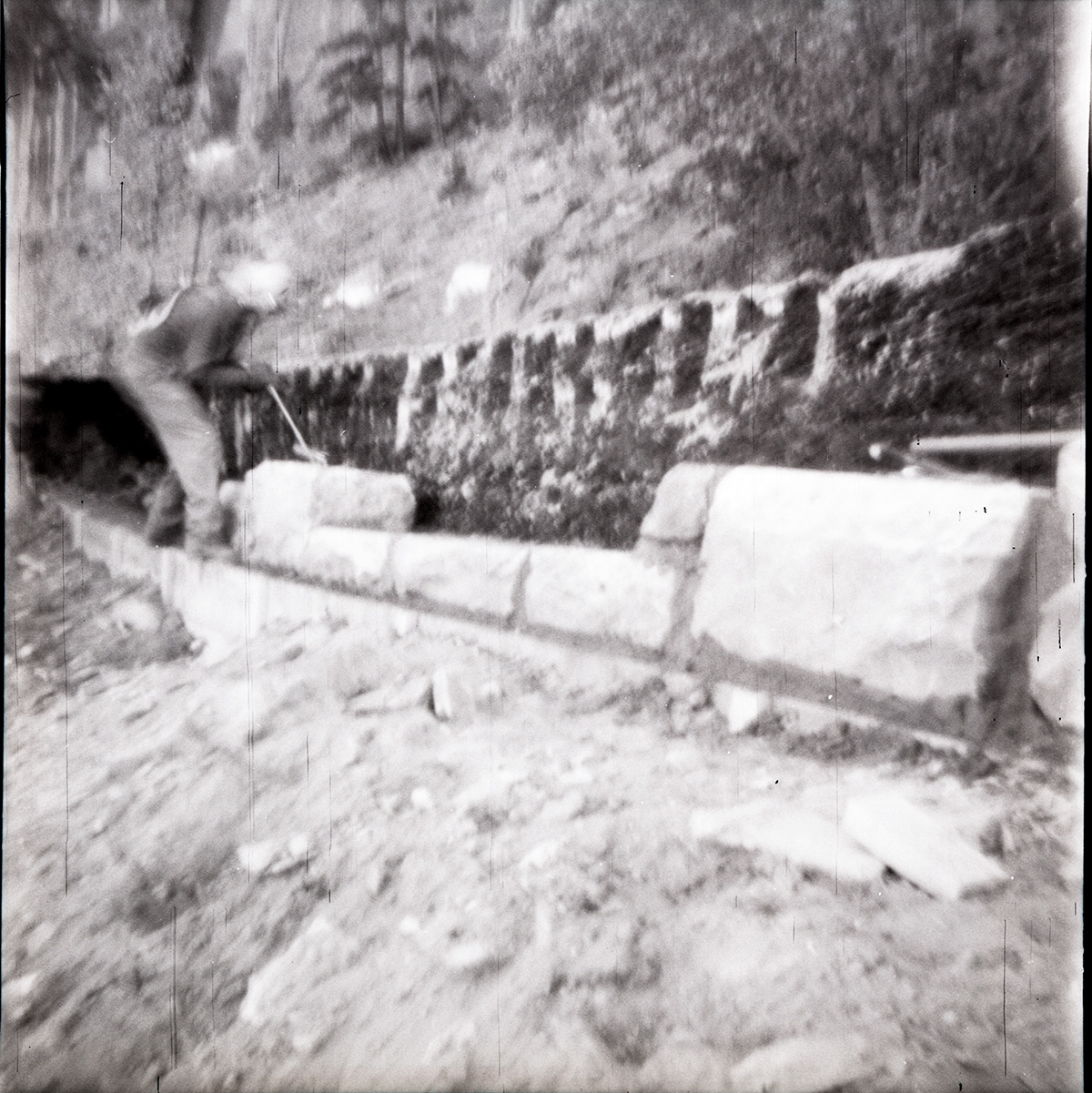 Man working on rebuilding rock retaining wall alongside road at the tunnel.