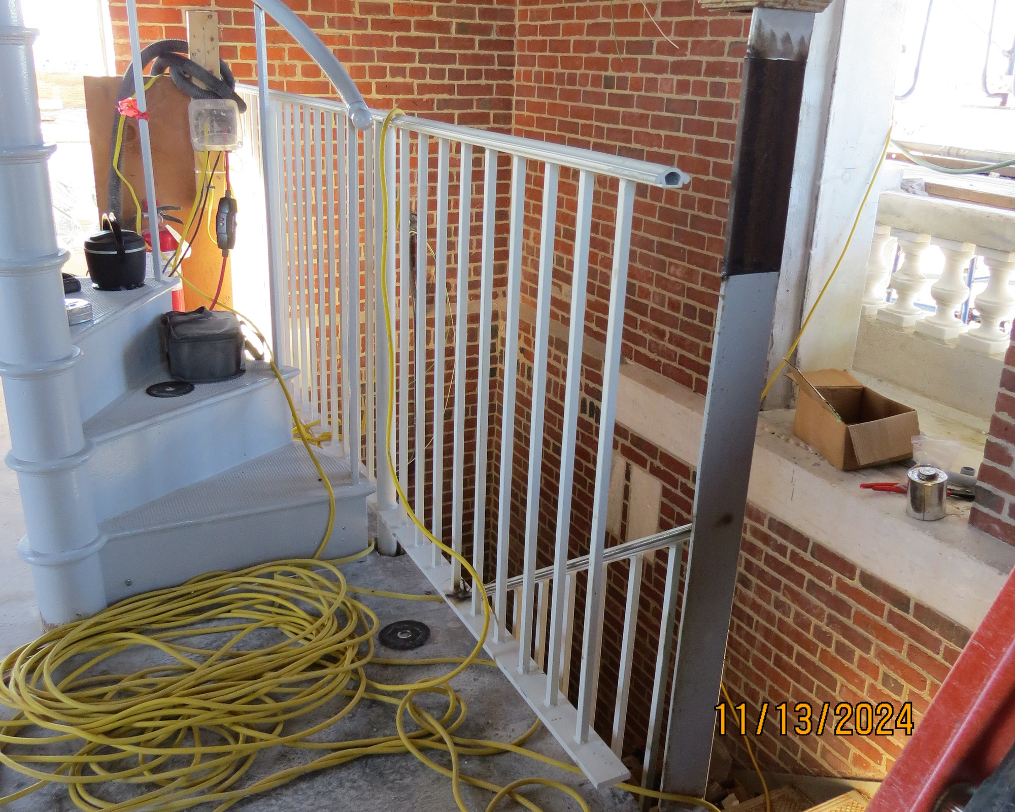 Installation of white handrails along the edge of a raised level. A curved staircase is to the left of the handrails. 