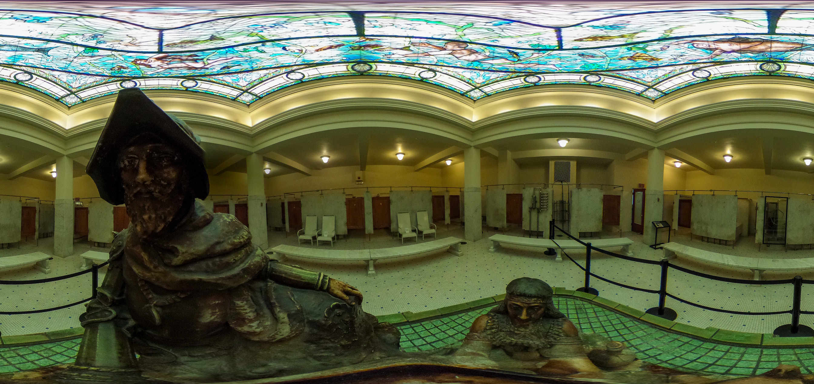 A stature of a native american offering water to a traveling man with seating for lounging around the statue 