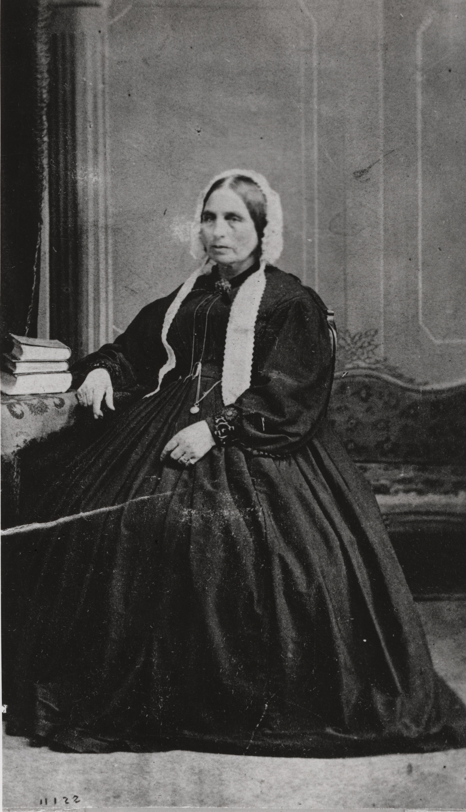 Black and white photograph of a seated woman in floor length black dress with wide skirt