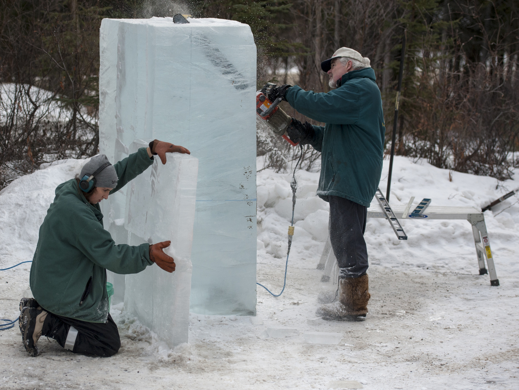 people work on sculpting an ice block