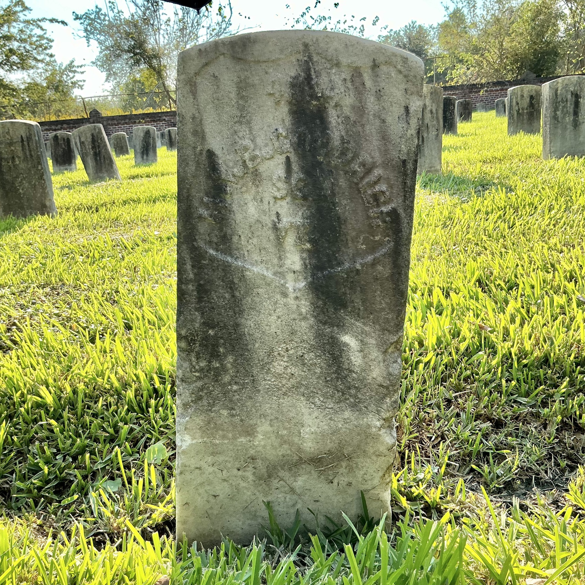 Front of historic upright marble headstone with recessed shield face.