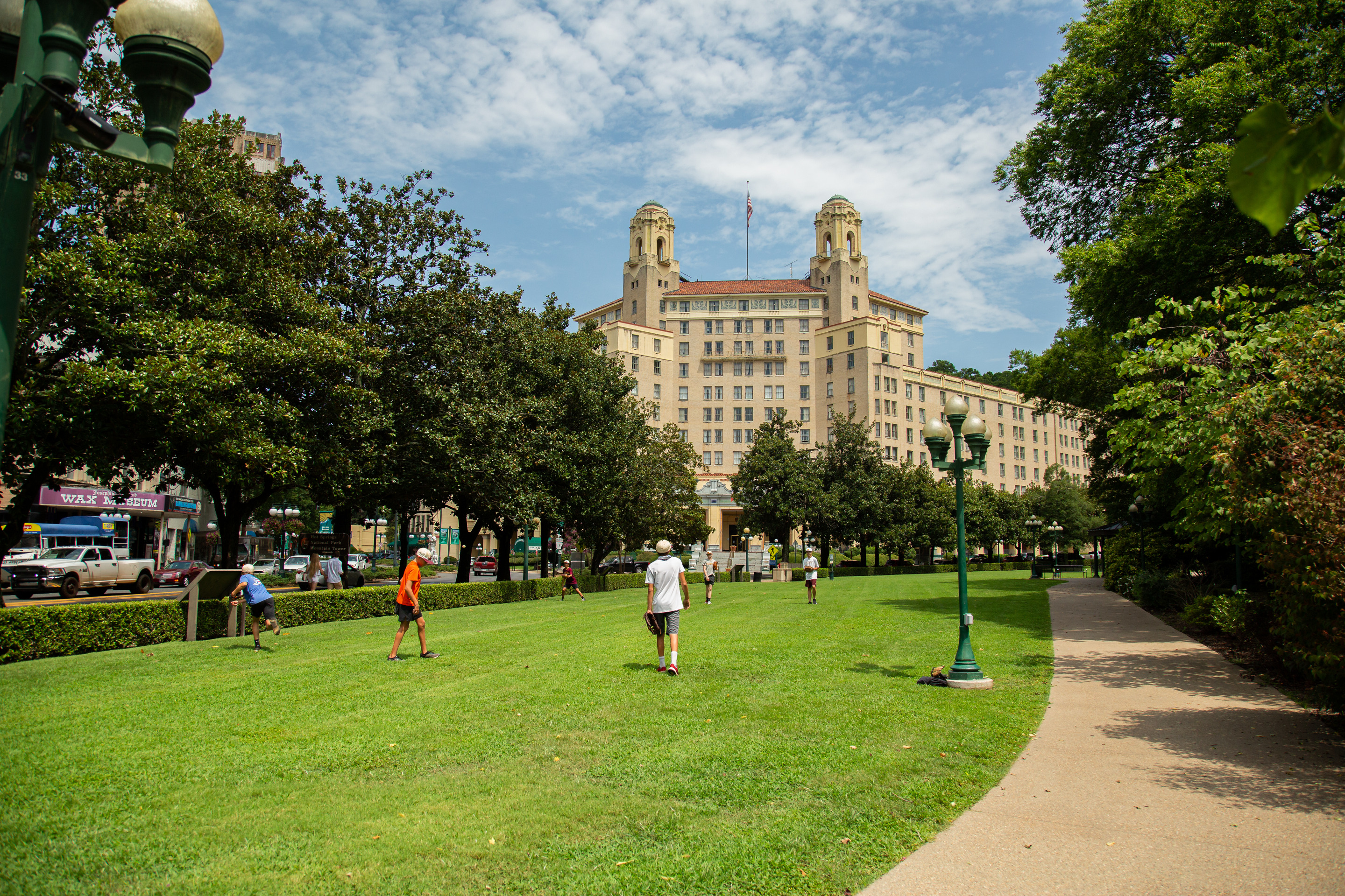 A group of boys practices throwing baseballs on the open lawn with a large two pillared hotel behind them. 