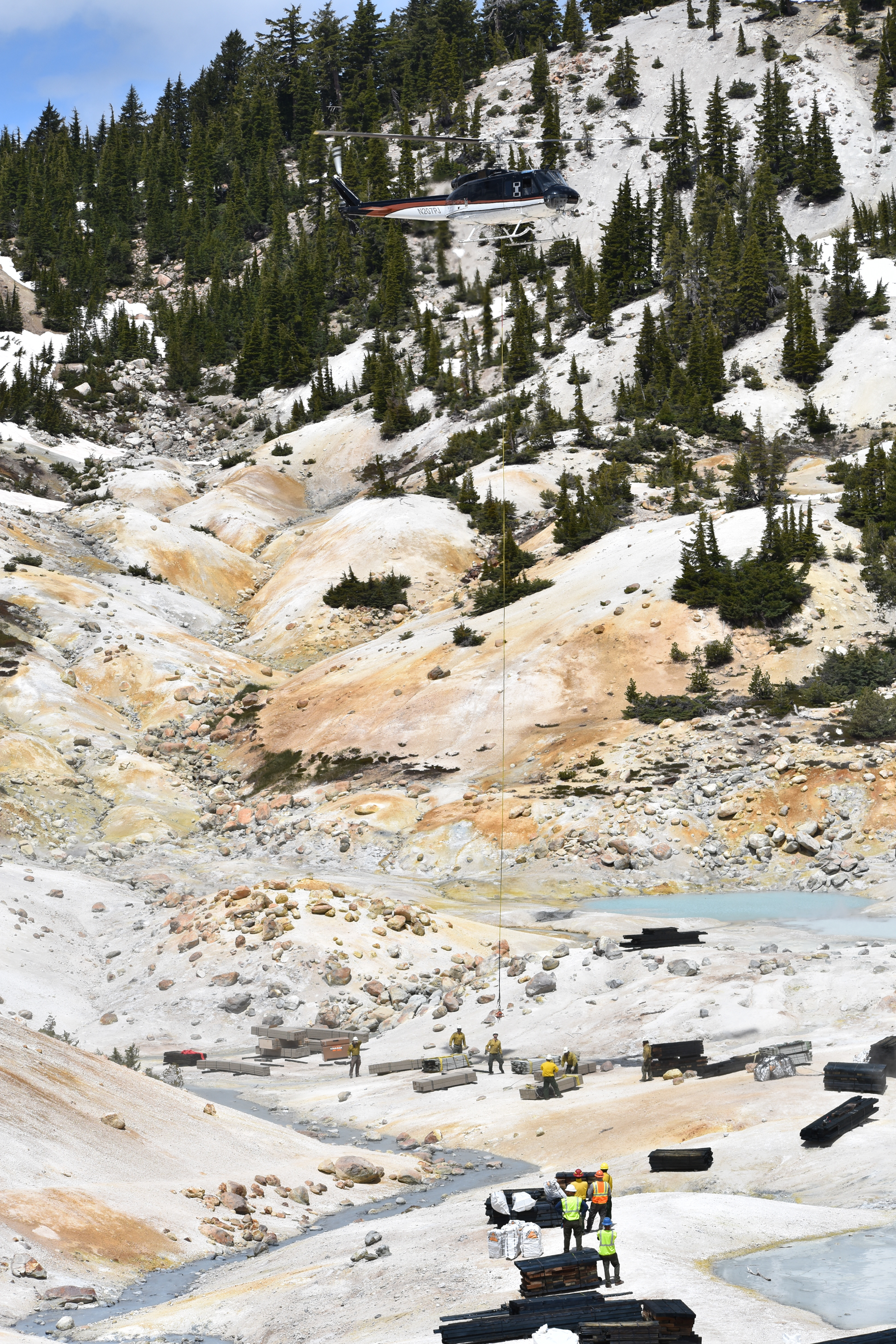 A long cable hangs from a helicopter hovering over a hydrothermal basin