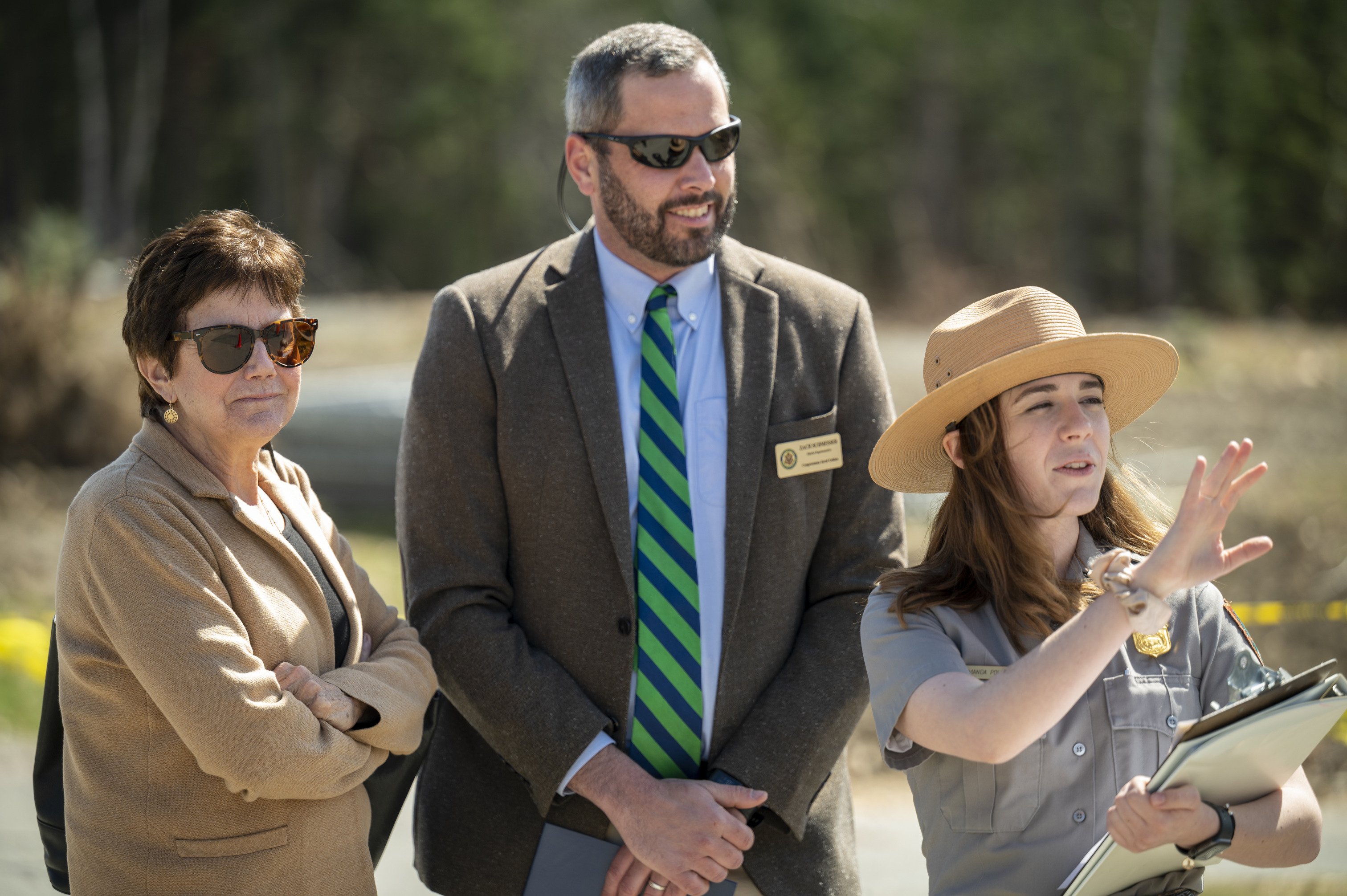 A park ranger gestures in front of her and a woman and man pay attention to her instructions.