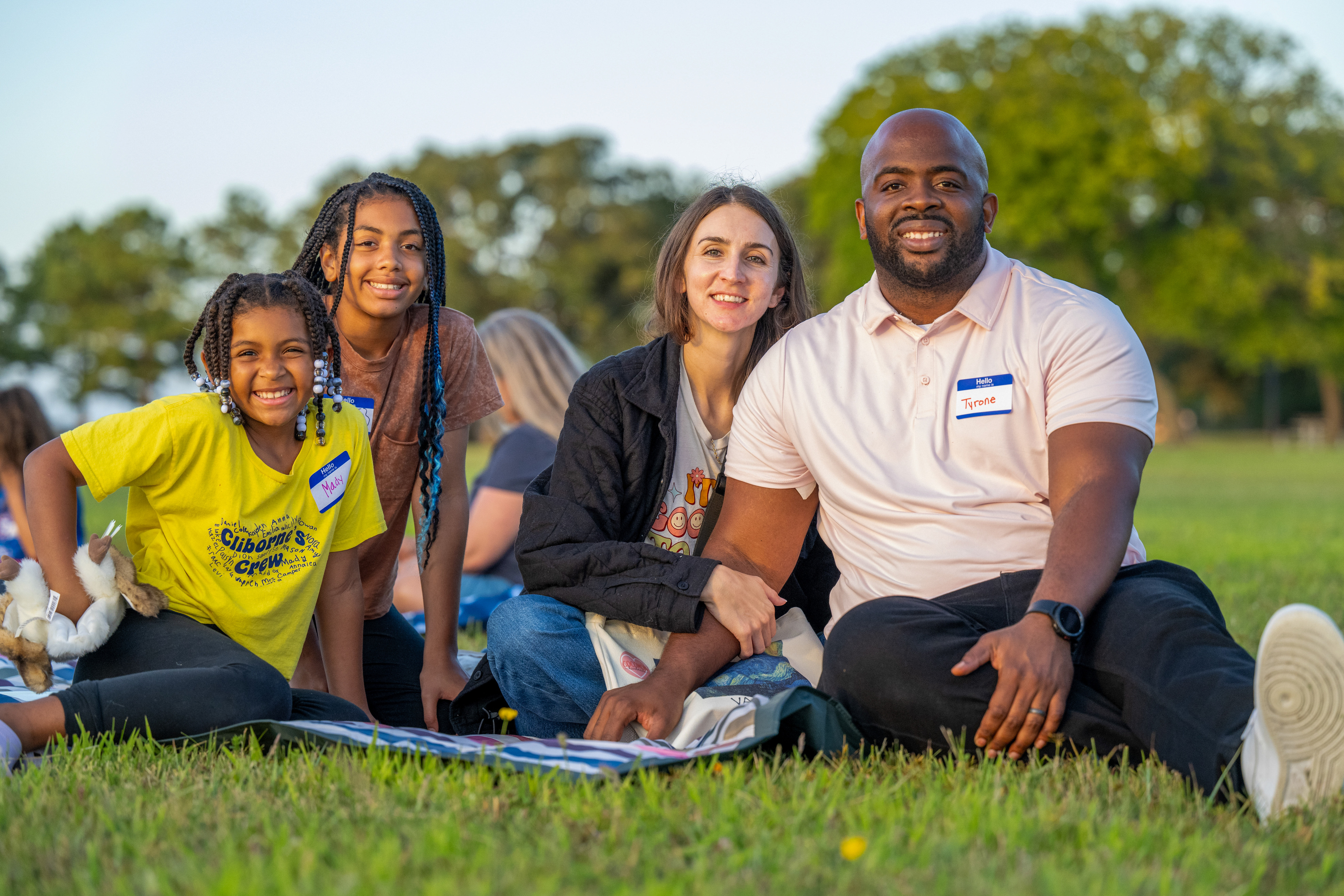 A family of two adults and two children on a picnic blanket pose for a photo.