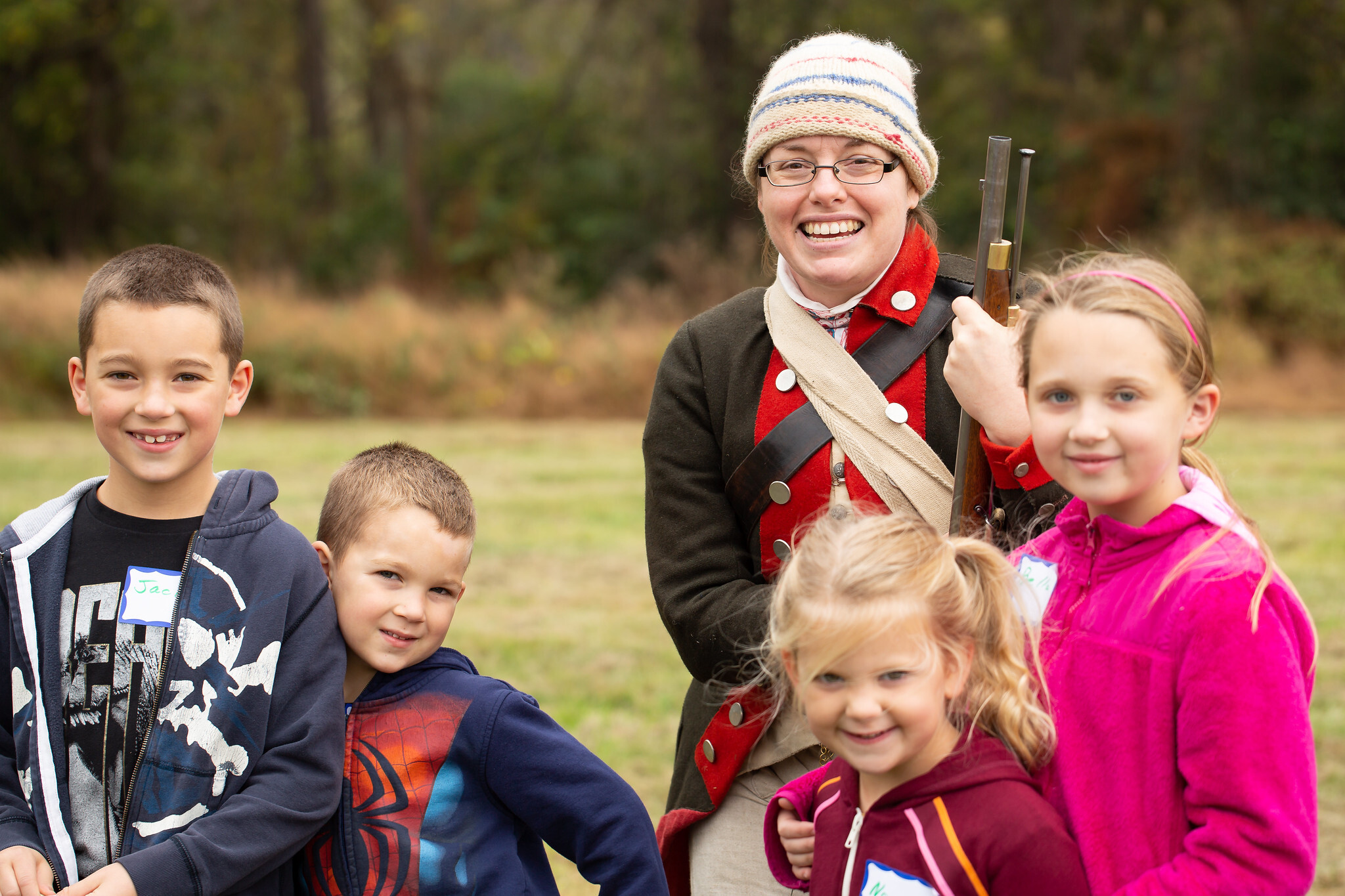Four children and one woman dressed as a Continental Army soldier smile at the camera