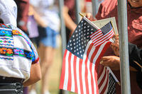 3 US flags in close proximity are in tight focus. Behind them is a new US citizen certificate, and a commotion of unfocused human forms.