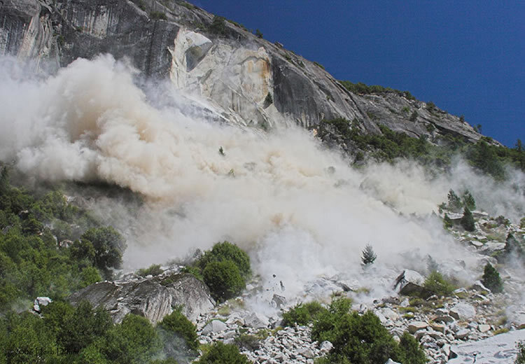 A close perspective of a brown and white dust cloud with boulders actively fragmenting and crashing into the talus slope below.