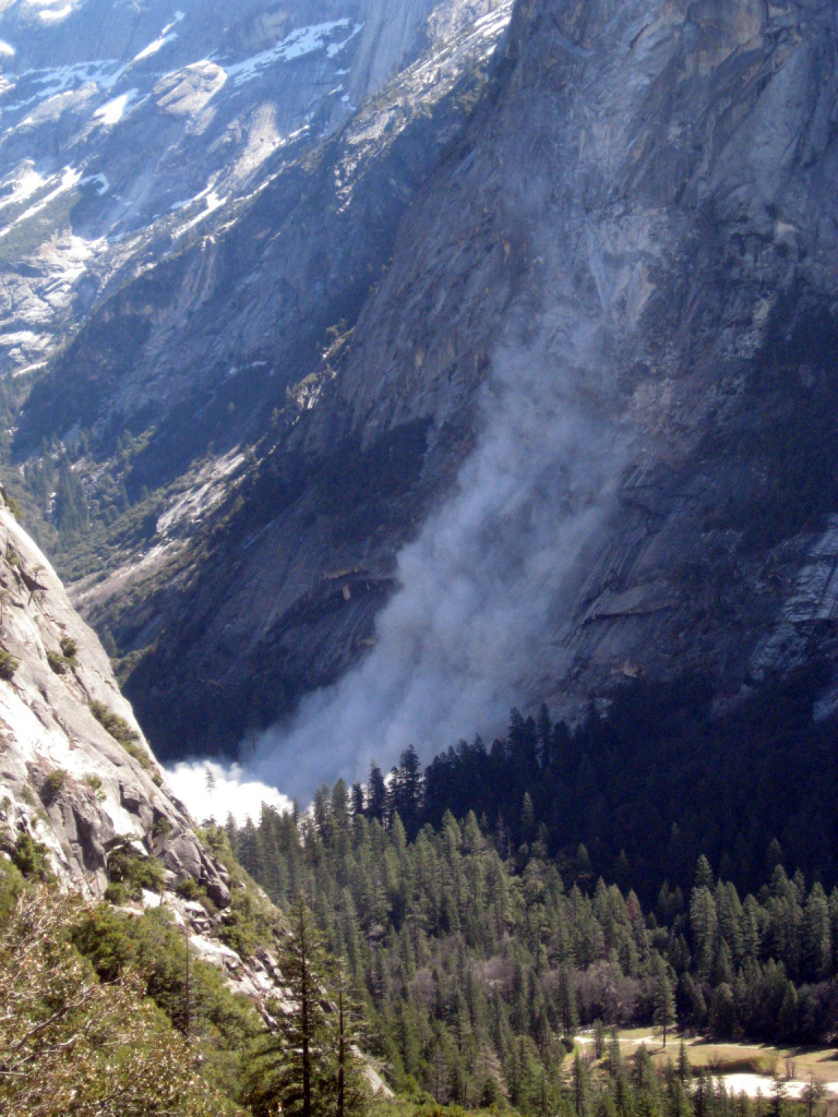 A dust cloud rises from the base of a steep cliff.