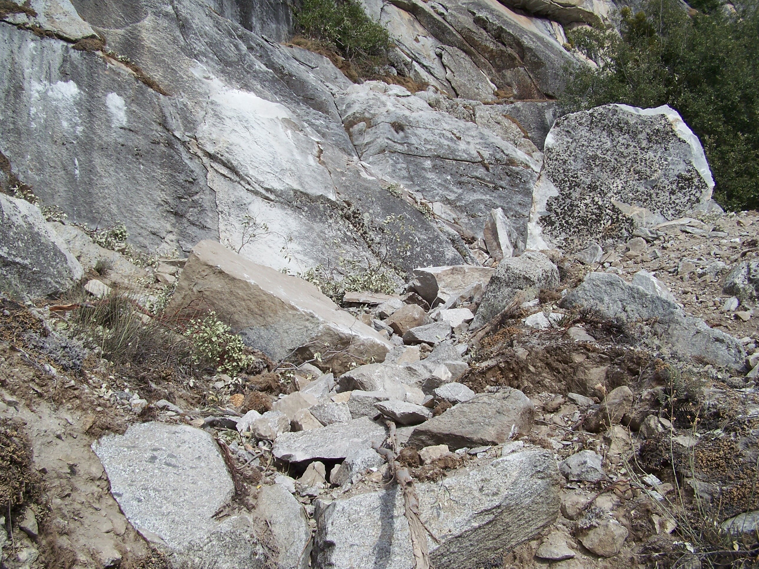 Fresh rock debris at the base of a rock wall and impact marks on the wall.