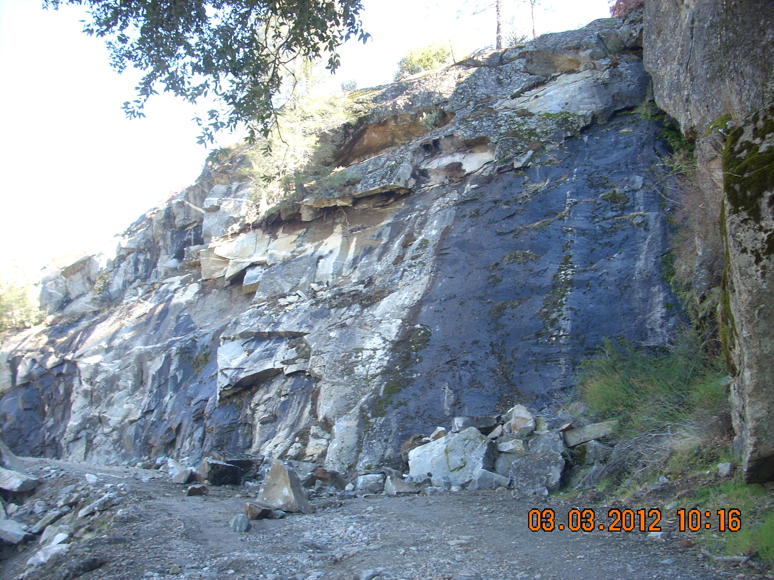 Several small boulders on a gravel road next to a steep rock face.