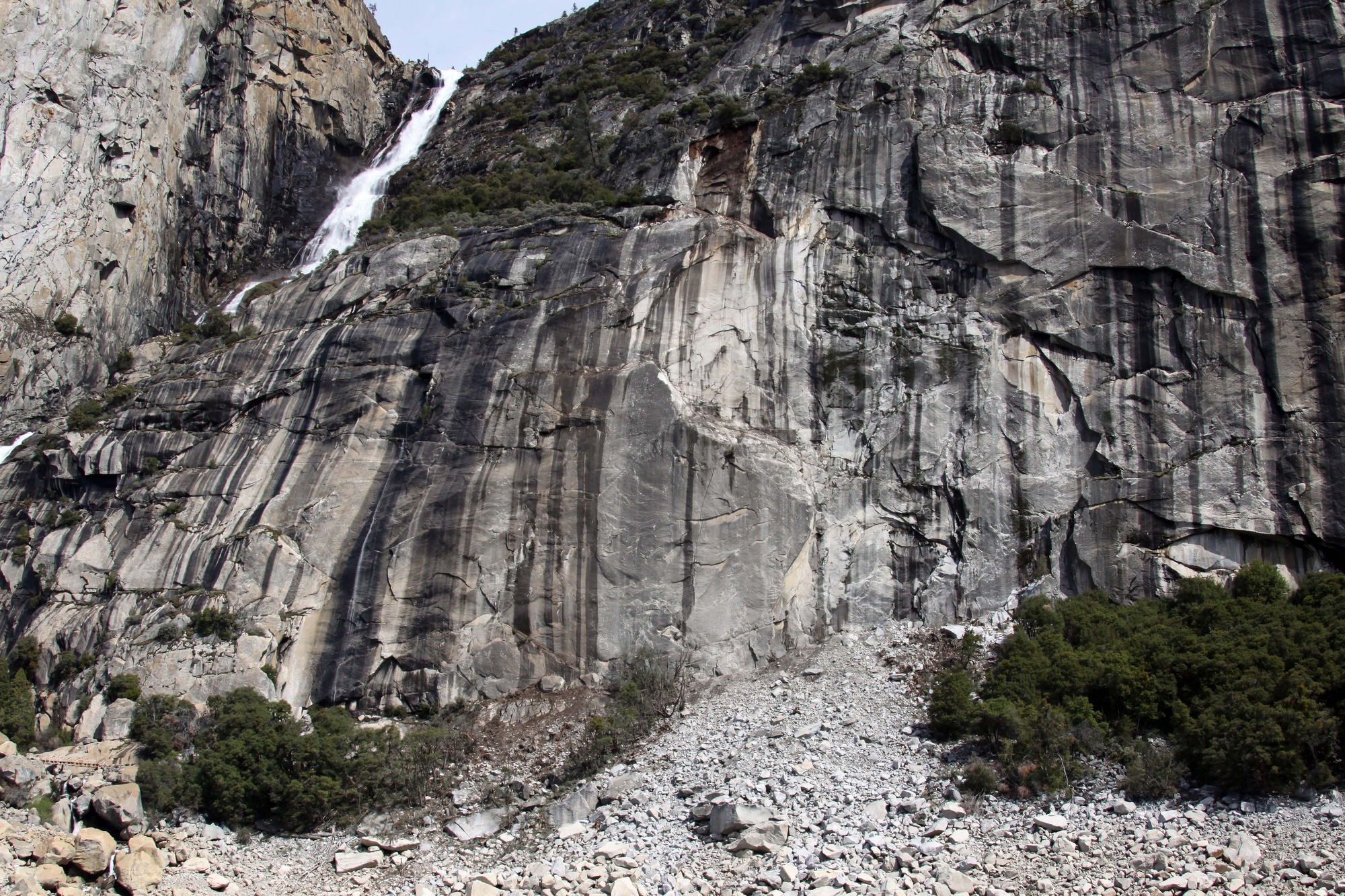 A large impact zone beneath the source area at the bottom of a steep rock cliff, separated into two areas by a strip of intact trees.