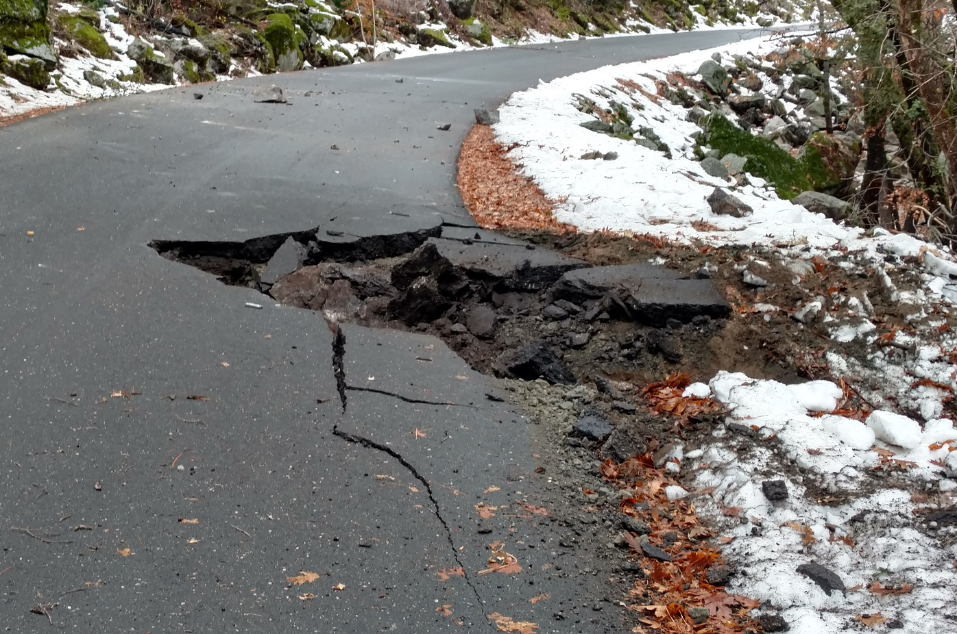 A hole punched into a paved road by a rock fall boulder, spanning one lane.