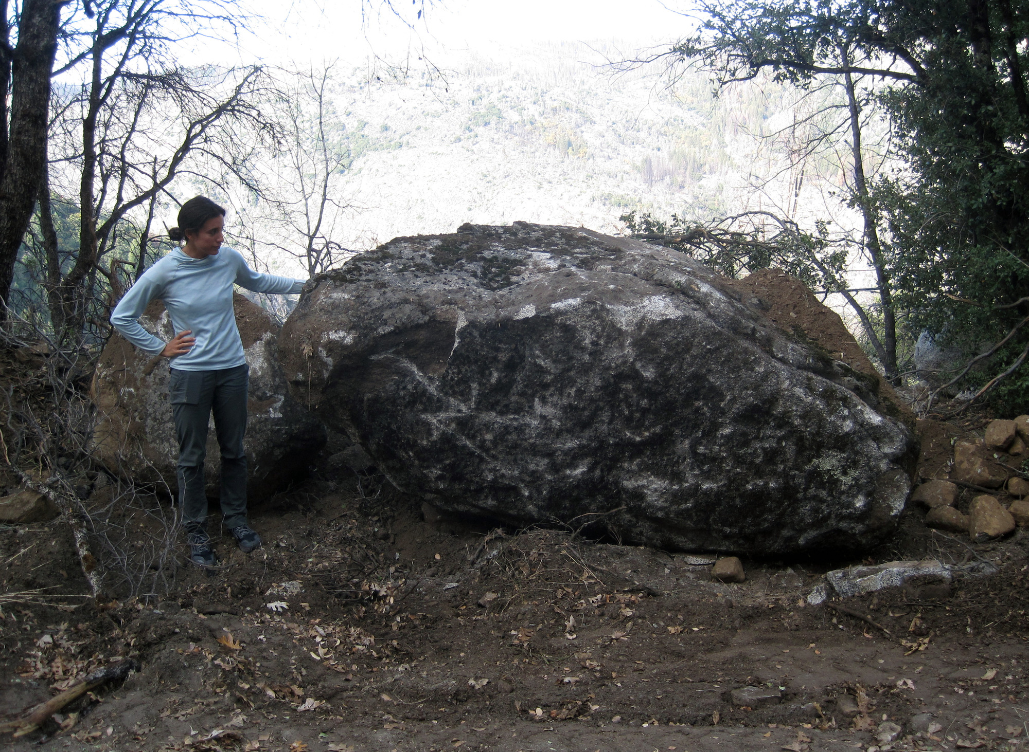 A person stands next to a large boulder.