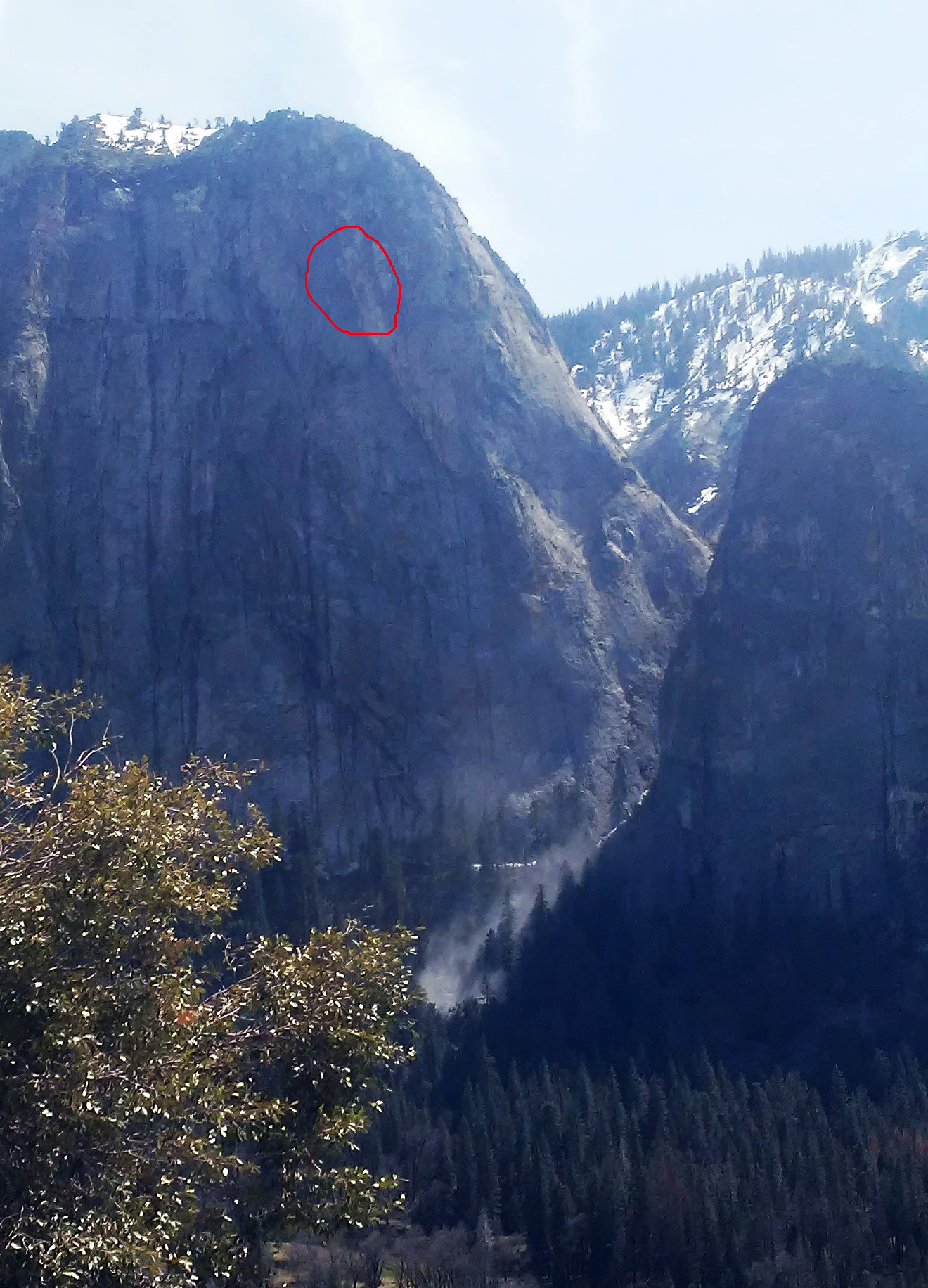 Photo with a red circle indicating the location of a rock fall source area on a steep cliff face and a small dust cloud near the valley floor.