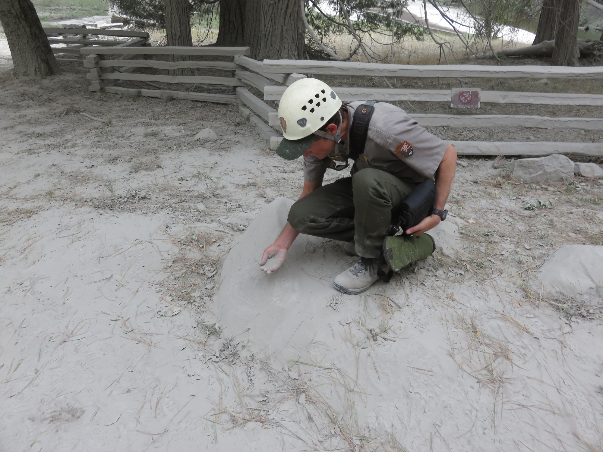 A person bent over, scooping up rock dust that is completely covering the ground around them in a deposit up to 3 cm thick near the base of the talus slope.
