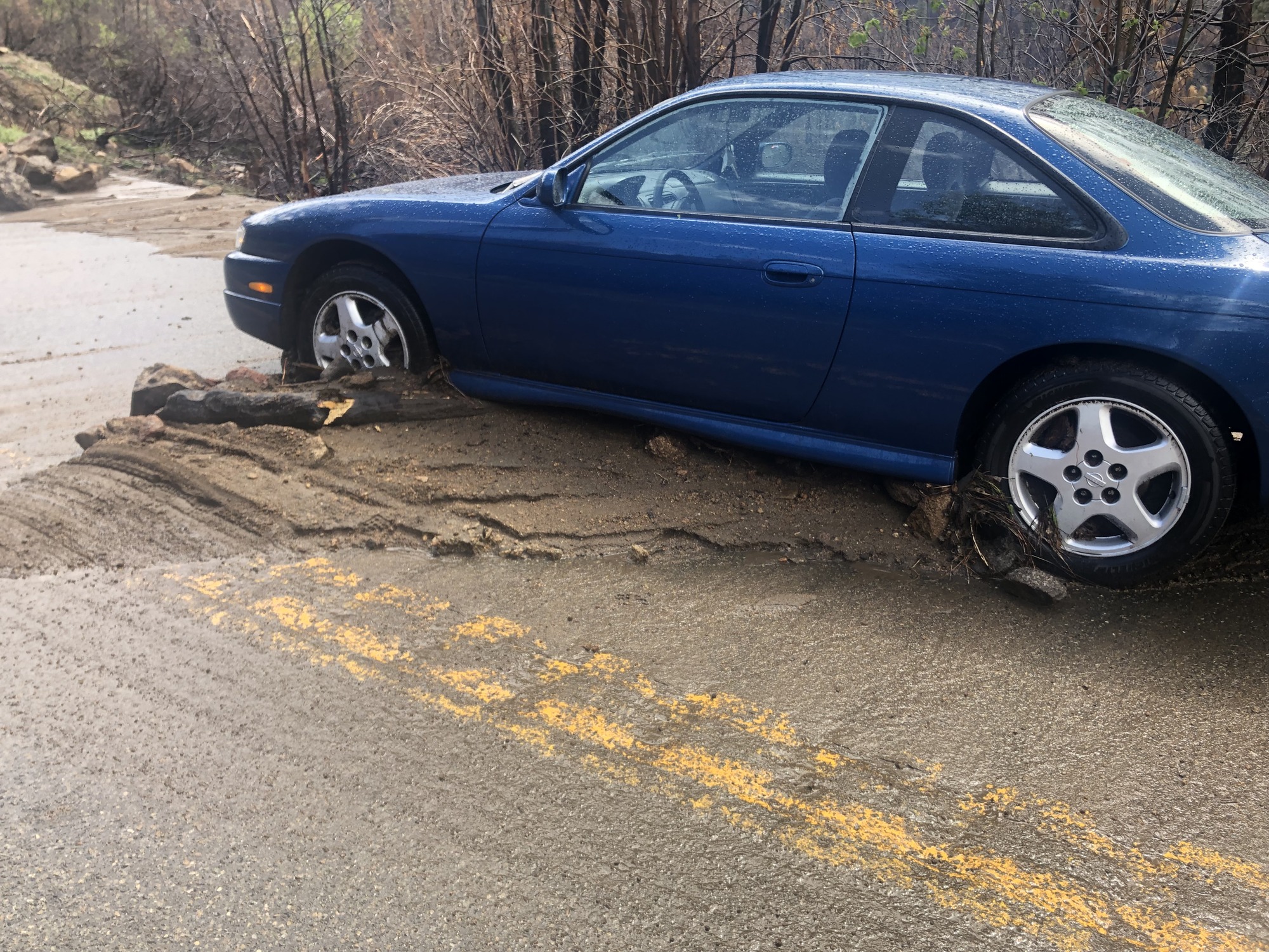 A low-clearance sedan-type vehicle stranded in a mud deposit and abandoned on the road.