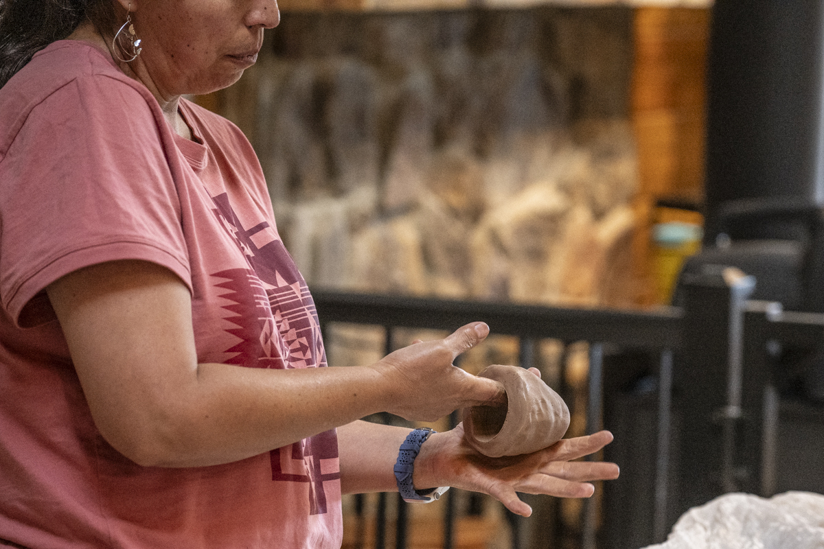 A woman molds and sculpts a piece of wet clay into a small pot.