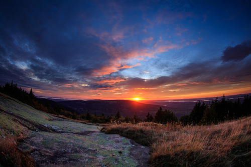 Vivid chromatic display of colors at sunset. Granite cliff at bottom of photo, clouds and blue sky at top.