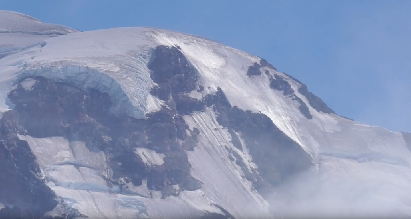 Light, misty clouds swirl around the glaciated summit of Mount Rainier.