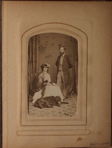 Black and white photograph of man and woman with black dog sleeping at the woman's feet.