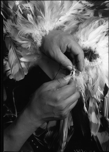 Le-me weaving feathers into a ceremonial apron.