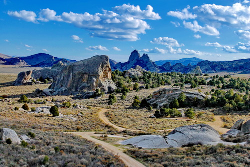 Granite monoliths tower above sagebrush desert and below a partly cloudy blue sky