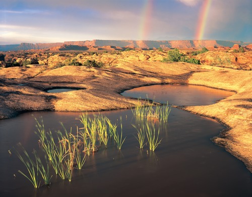 potholes filled with water with a double rainbow in the background
