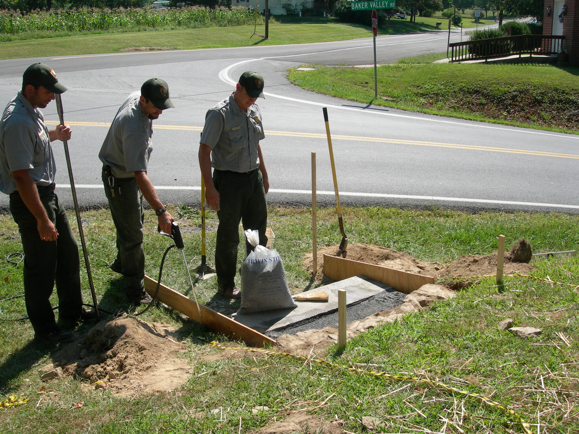 Three men in NPS uniforms stand in front of a granite step. One holds a pry bar. One holds a spray nozzle and the third has a large bag in front of him.