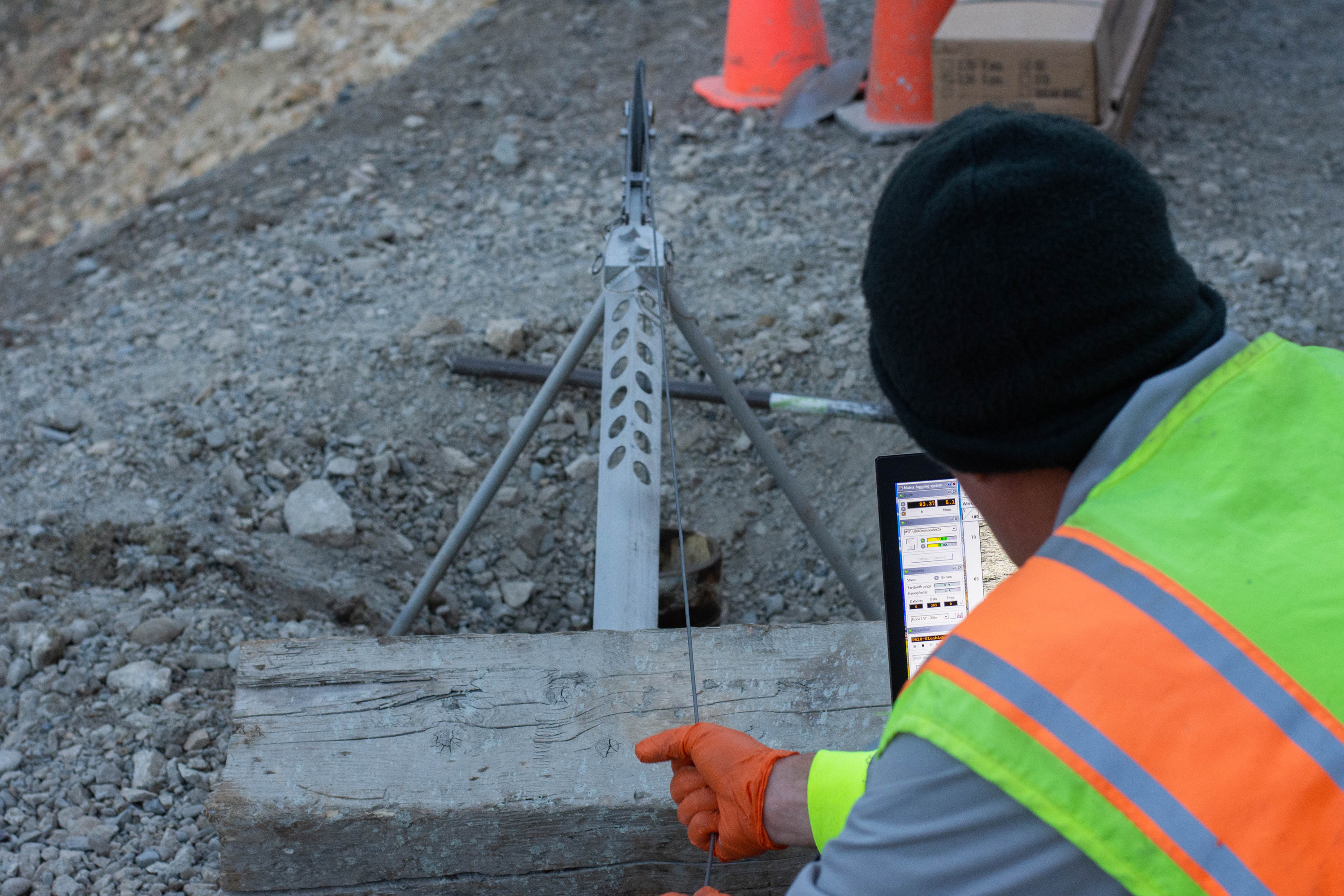 man looking at a laptop connected to a sensor of some kind in a hole in the ground
