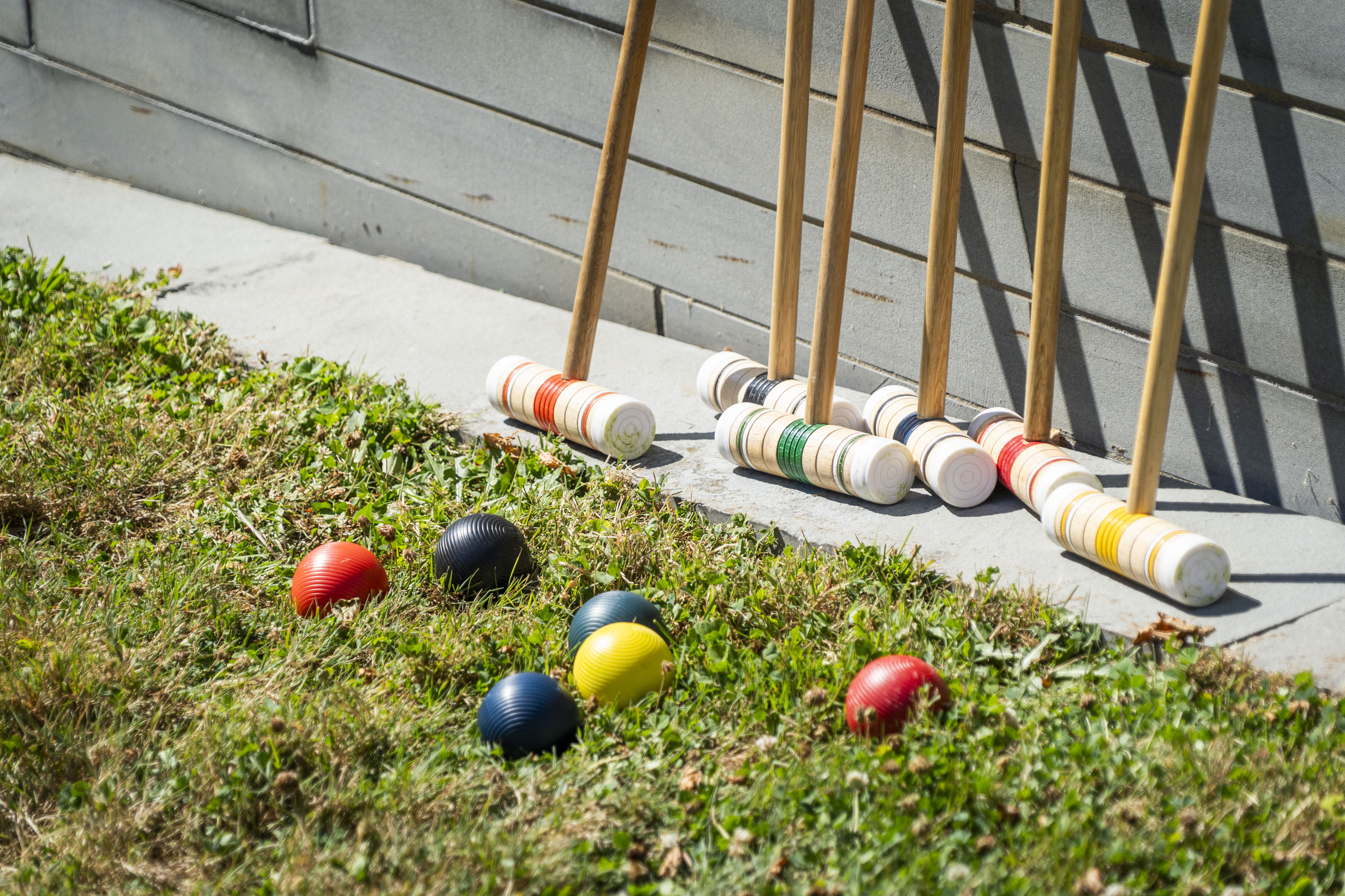 Croquet mallets and balls lined up in the grass against a stone wall