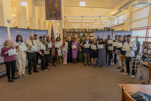 Several people standing up and posing with pieces of paper held in front of them.