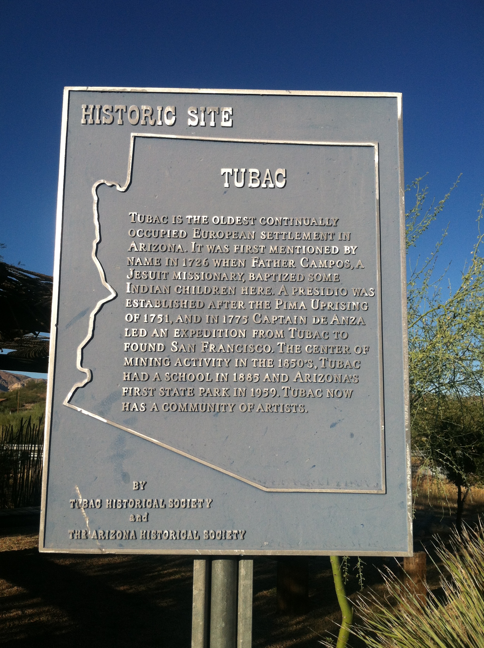 A sign showing the outline of the state of Arizona that reads, "Tubac - Tubac is the oldest continually occupied European settlement in Arizona. It was the first mentioned by name in 1726 when Father Campos, a Jesuit Missionary, baptized some Indian children here. A presidio was established after the Pima Uprising of 1751, and in 1775 Captain de Anza led an expedition from Tubac to found San Francisco. The center of mining activity in the 1850's, Tubac had a school in 1885 and Arizona's first state park in 1959. Tubac now has a community of artists."