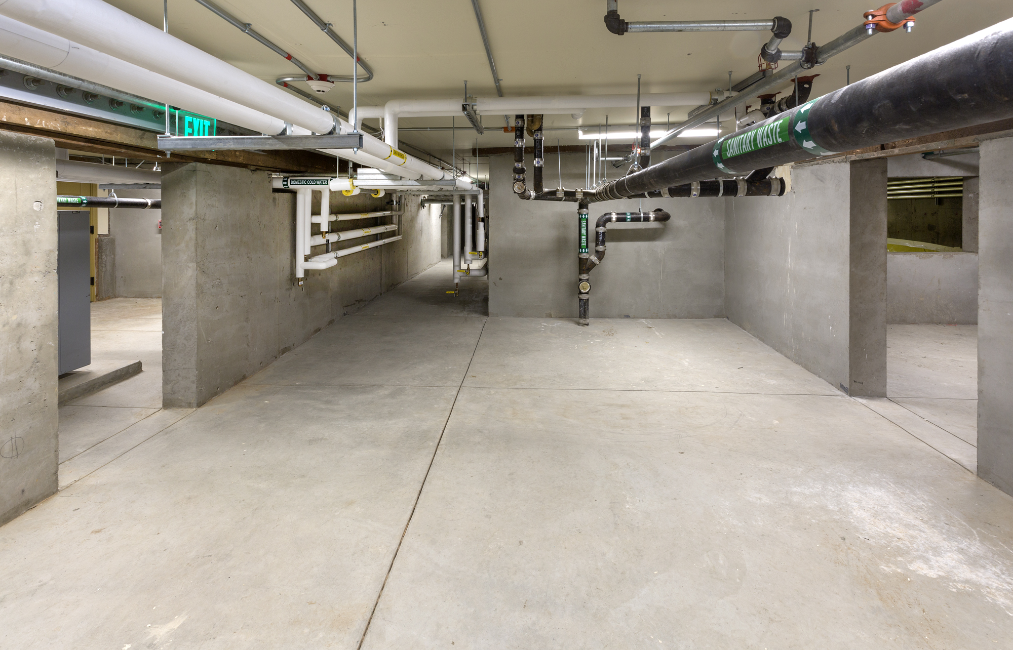 A basement room with concrete floor and walls with pipes going along the ceiling.