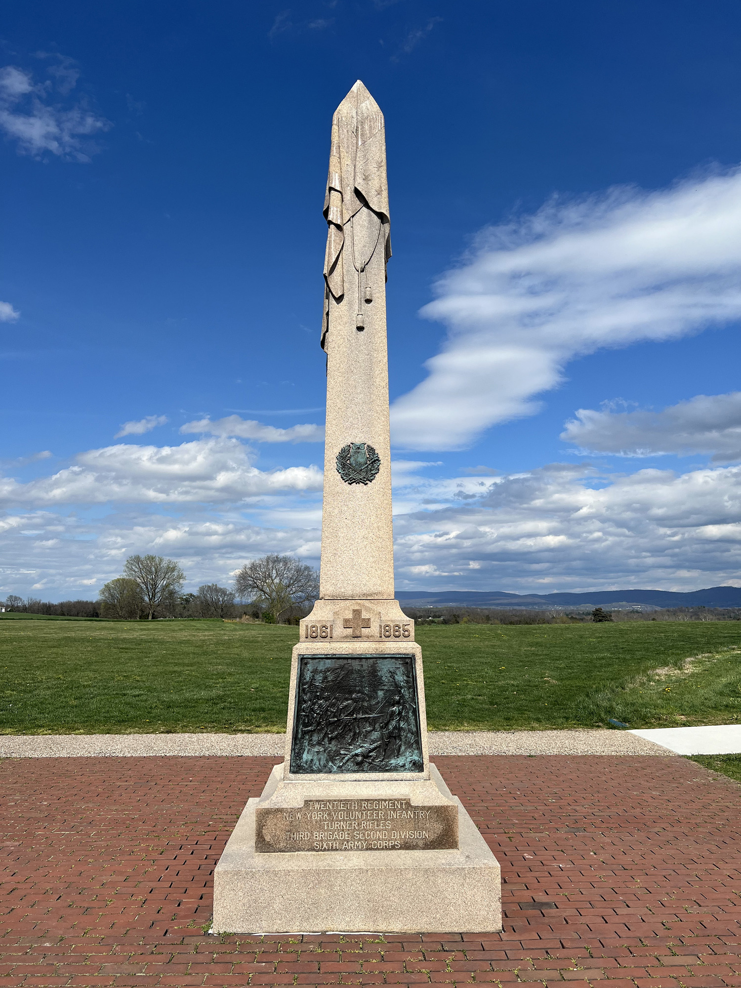 obelisk monument with carved flag draped over it blue sky white clouds in background 