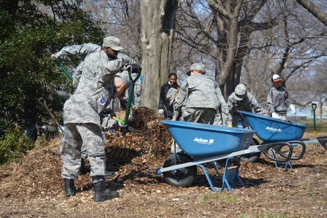 Many servicemembers in uniform use shovels and pitchforks to spread mulch around trees. 