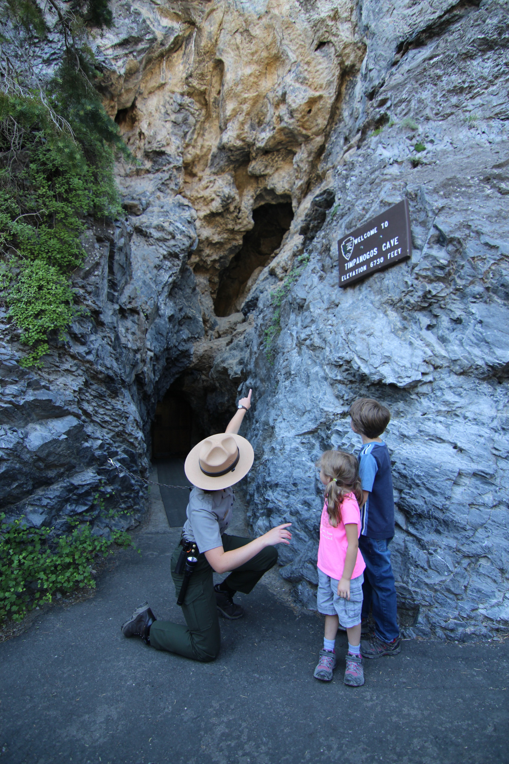 A ranger pointing at the cave entrance to two young children.