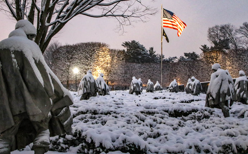 Statue of soldier covered in snow walking toward the US and POW flags