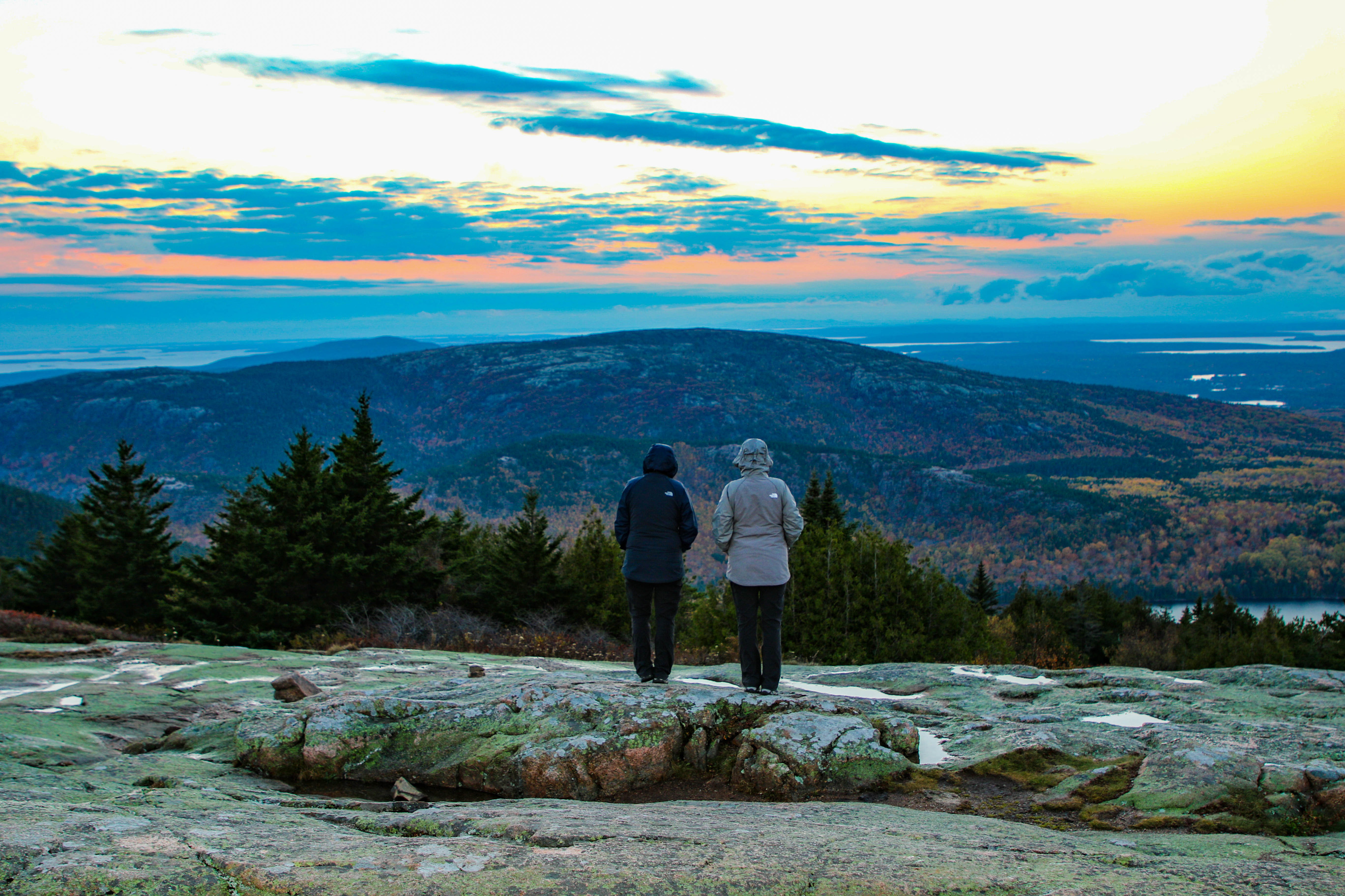 Two visitors watching the sunset from the top of a mountain