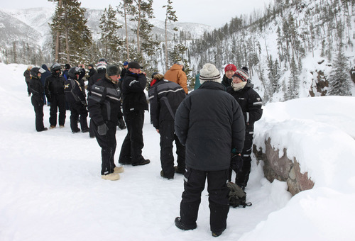 Group of people with snowsuits on standing near a rock wall which overlooks a waterfall which is out of view.