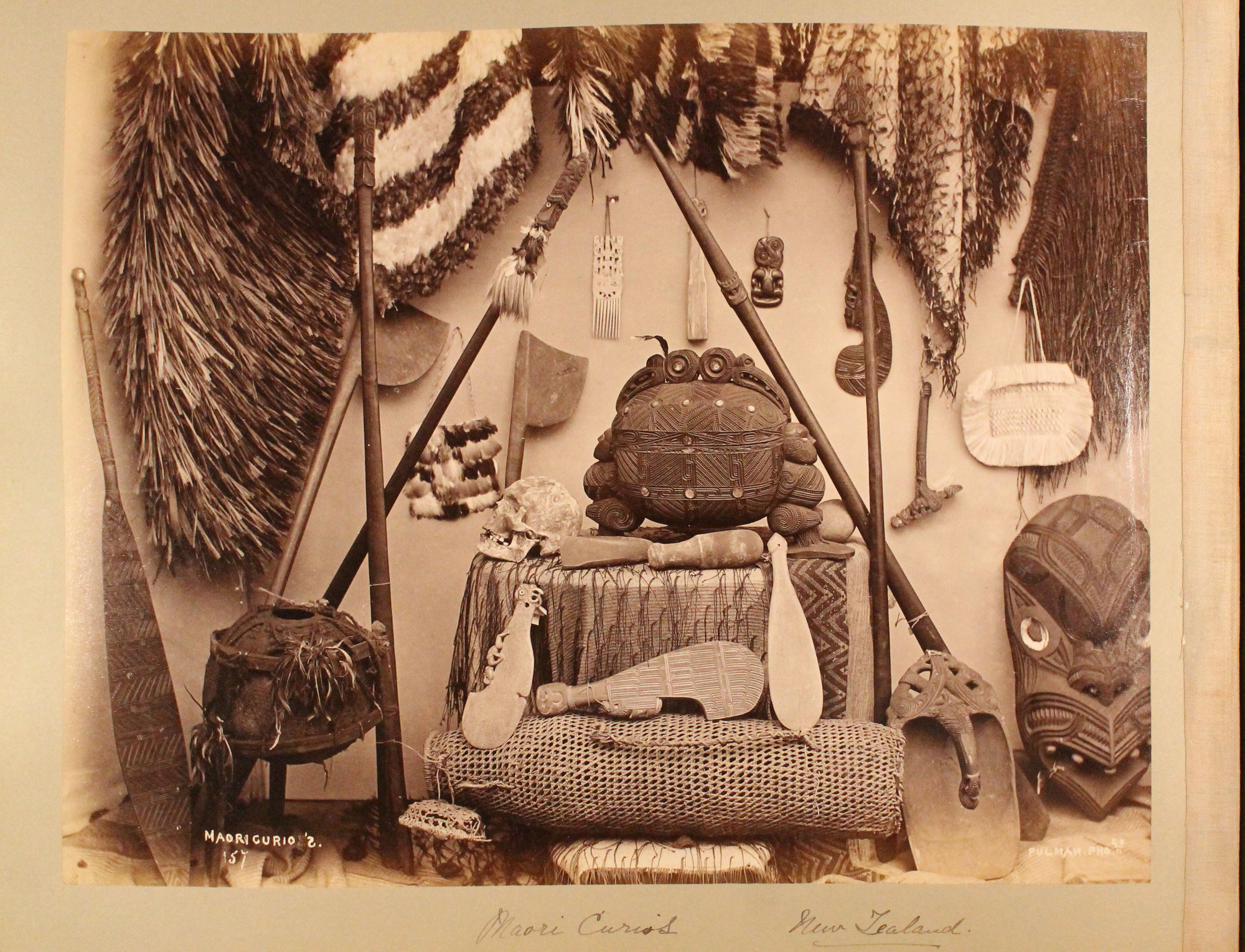 An assortment of Maori artifacts:  woven fiber cloaks, bags, a skull, pounding stones, and carved wooden paddles, staffs and containers.
