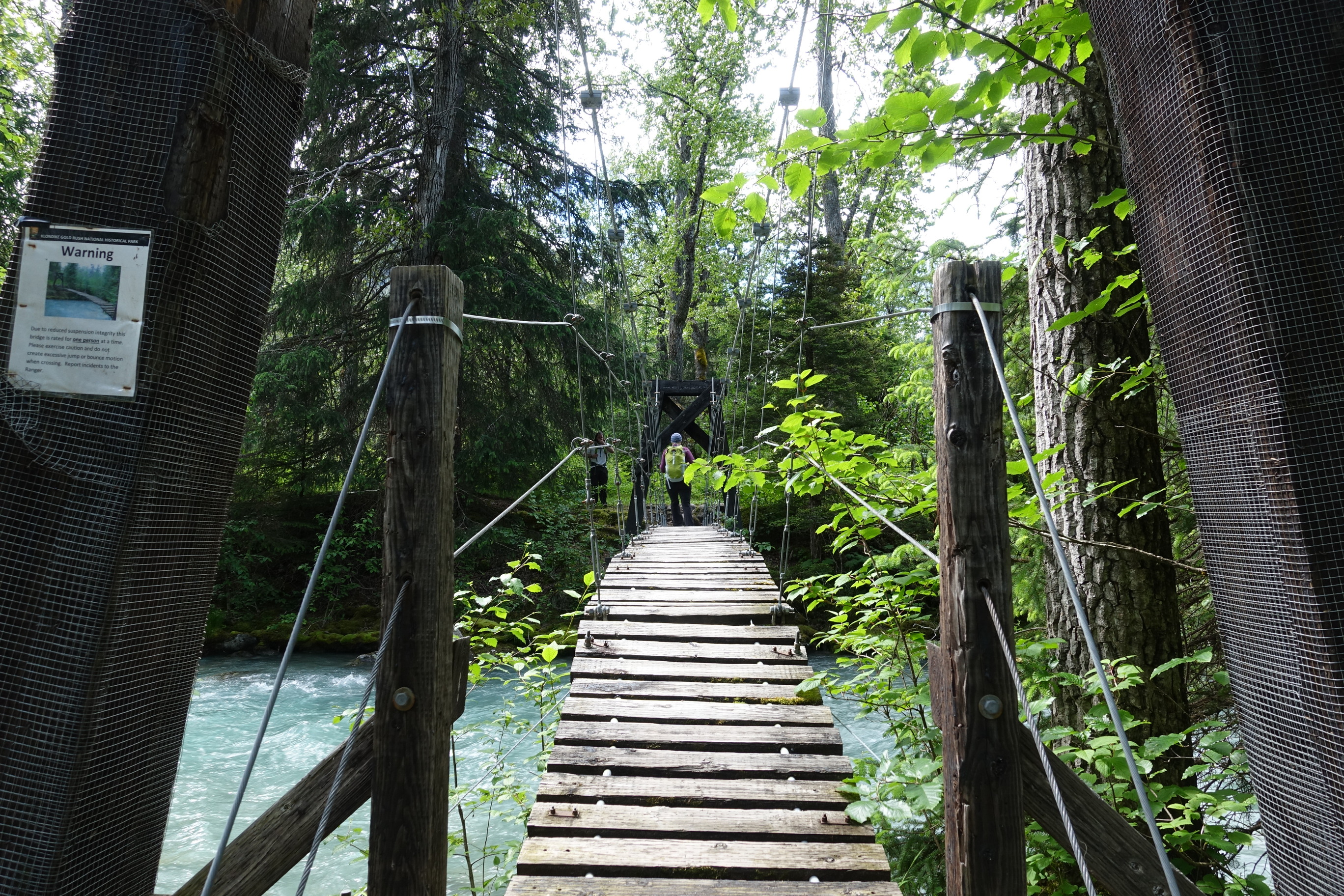 A suspension bridge at Canyon City. There is a sign reading "Warning: Due to reduced suspension integrity this bridge is rated for one person at a time. Please exercise caution and do not create excessive jump or bounce motion when cross. Report incidents to the Ranger."